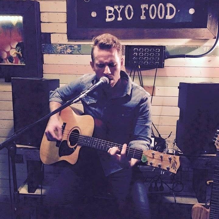 Dan Smith playing a seated acoustic set in a small Brisbane bar beneath a BYO Food sign